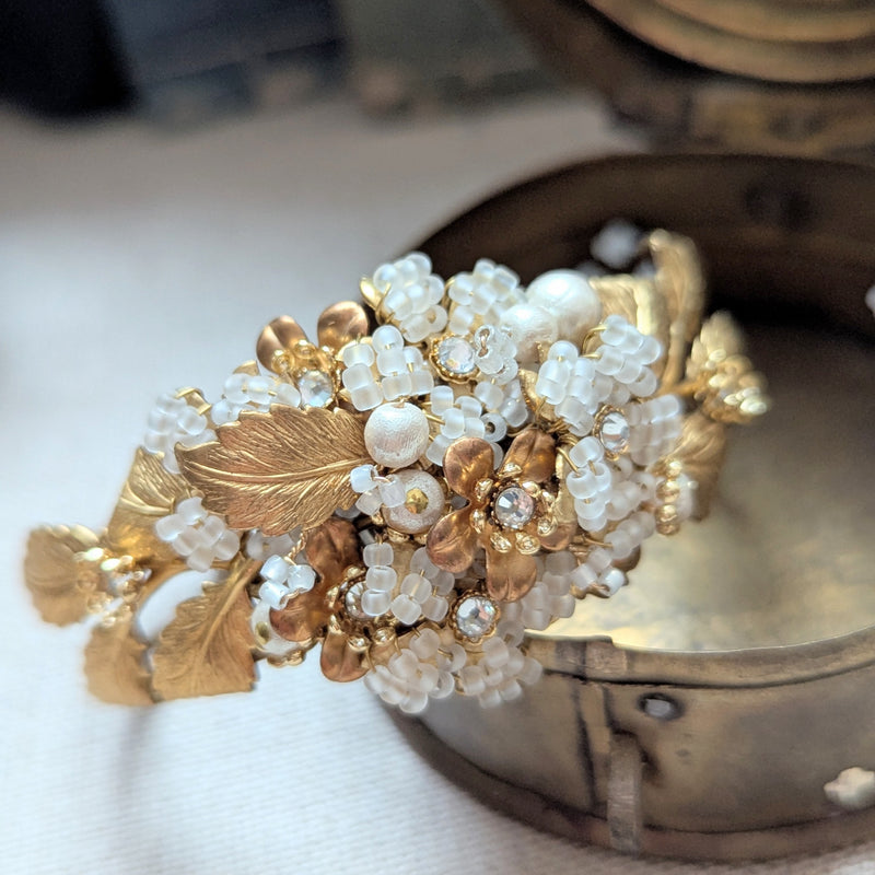 Large leaf shaped brass cuff bracelet with beaded, pearl, and crystal accent on a textured surface