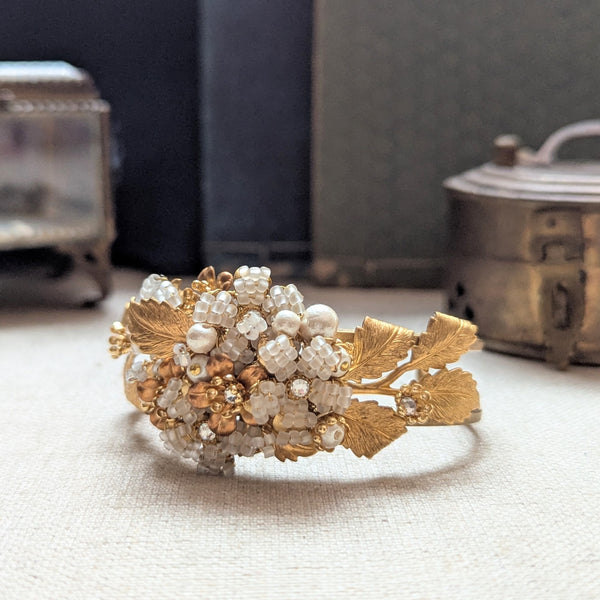 Large leaf shaped brass cuff bracelet with beaded, pearl, and crystal accent on a textured surface