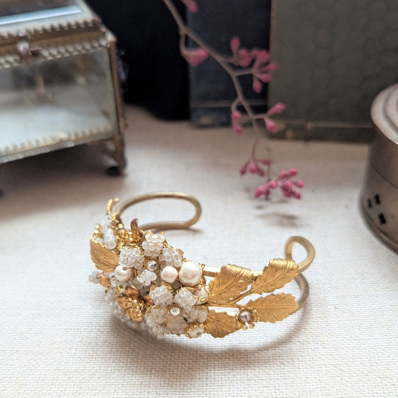 Large leaf shaped brass cuff bracelet with beaded, pearl, and crystal accent on a textured surface