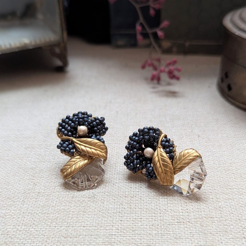 Pair of decorative earrings with black beads and gold leaves on a textured surface.