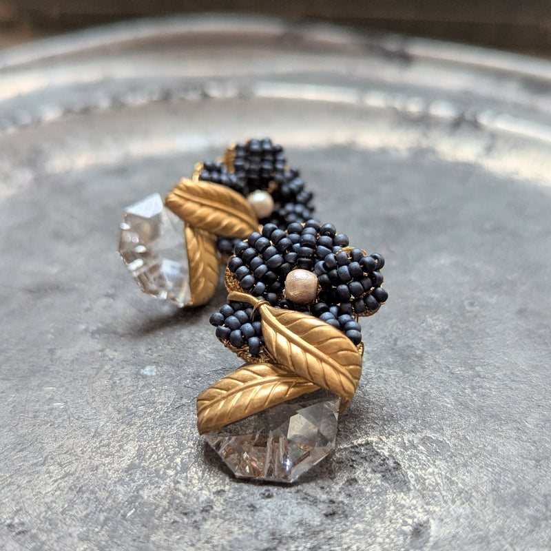 Pair of earrings with black bead and gold leaf design on a metallic surface