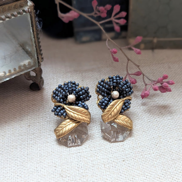 Pair of decorative earrings with black beads and gold leaves on a textured surface.
Monshiro Jewelry Japanese Sumire leaf earrings design floral nature inspired brass glass vintage handmade shop Boston sowa gift store boutique