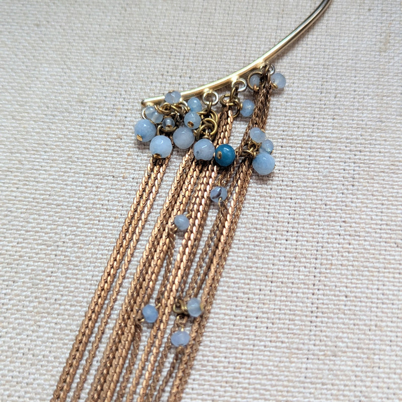 Brass ear cuff or ear hook with long  brass chain fringe and blue beads on a textured surface