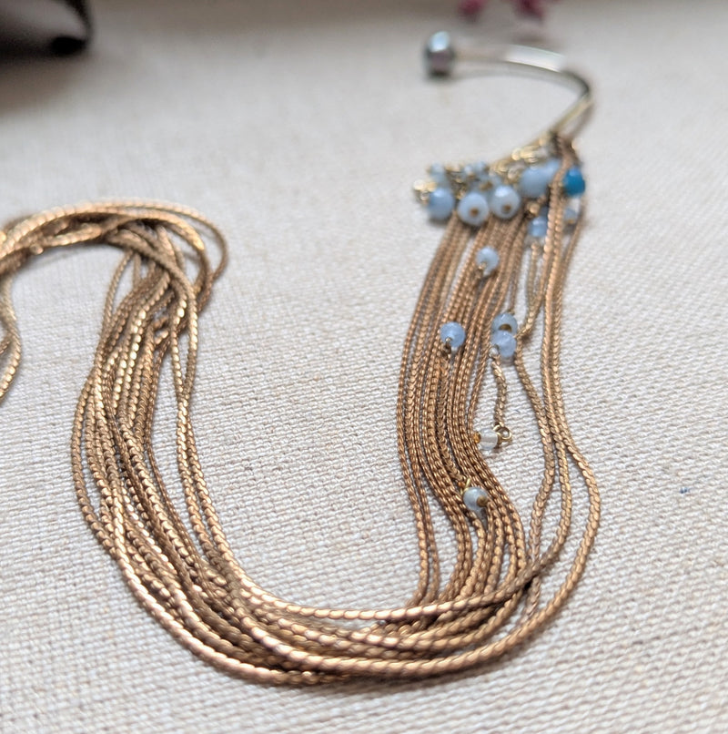 Brass ear cuff or ear hook with long  brass chain fringe and blue beads on a textured surface