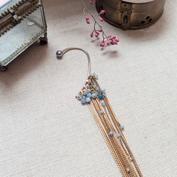 Brass ear cuff or ear hook with long  brass chain fringe and blue beads on a textured surface