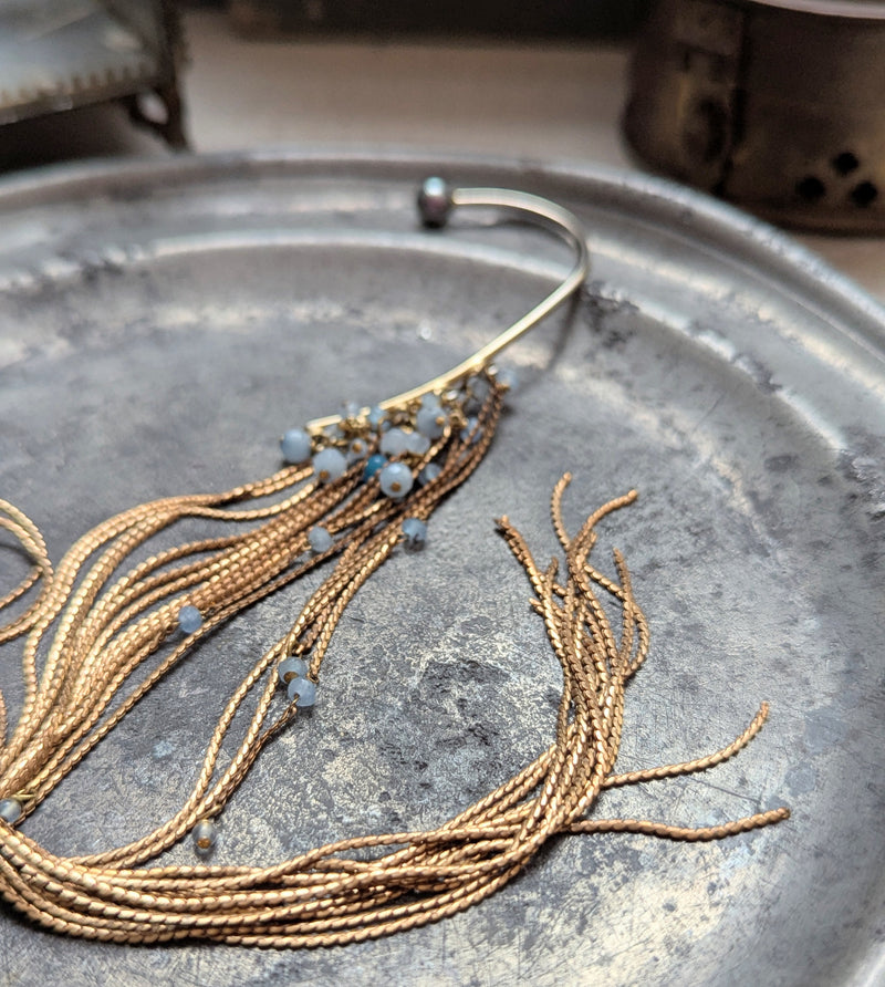 Brass ear cuff or ear hook with long  brass chain fringe and blue beads on a textured surface