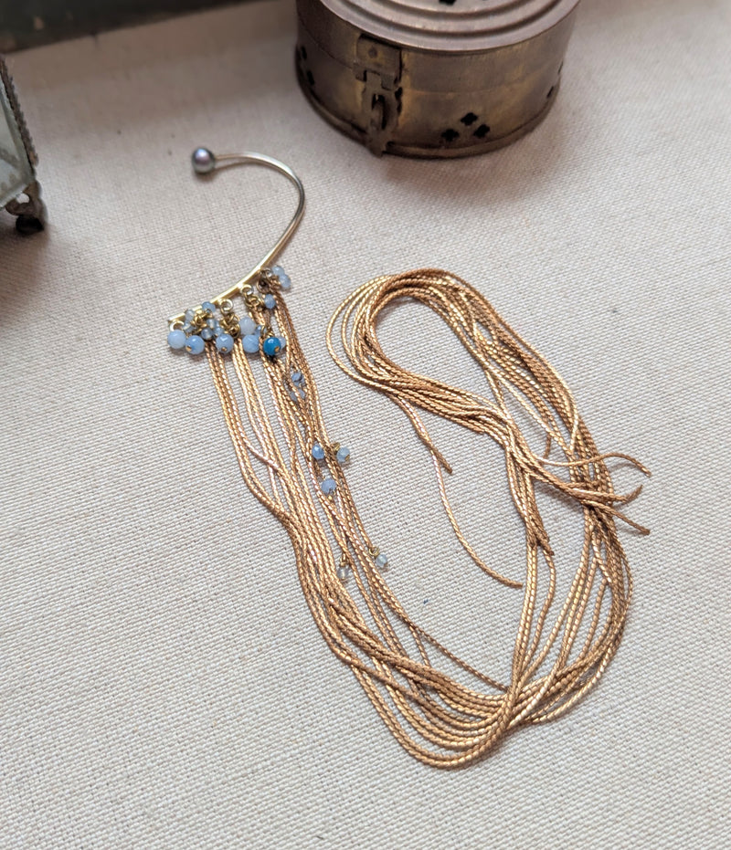 Brass ear cuff or ear hook with long  brass chain fringe and blue beads on a textured surface