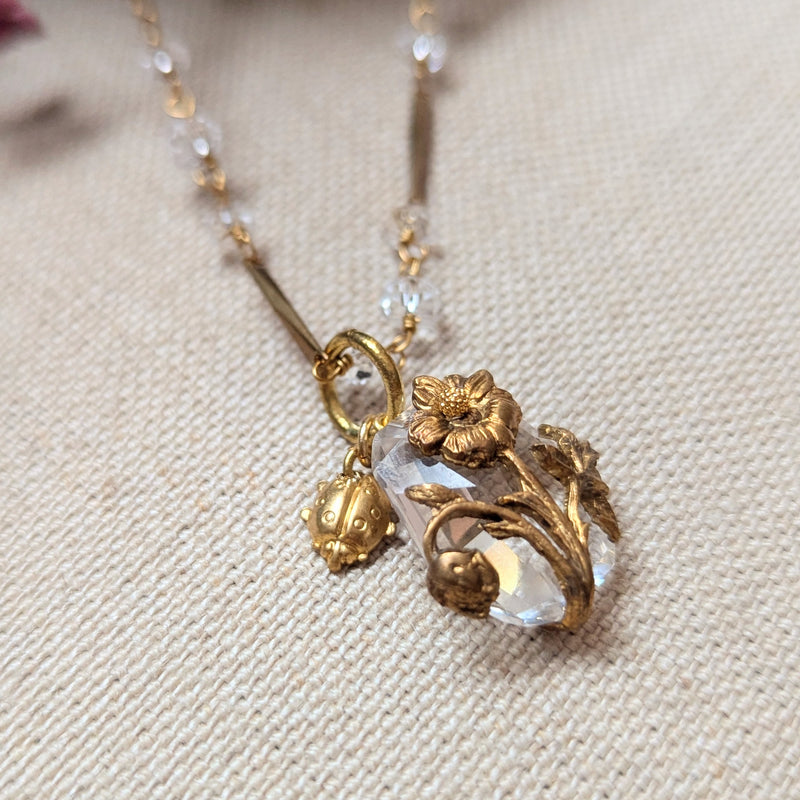 Brass necklace with crystal accents and a glass and brass Poppy pendant on a textured surface