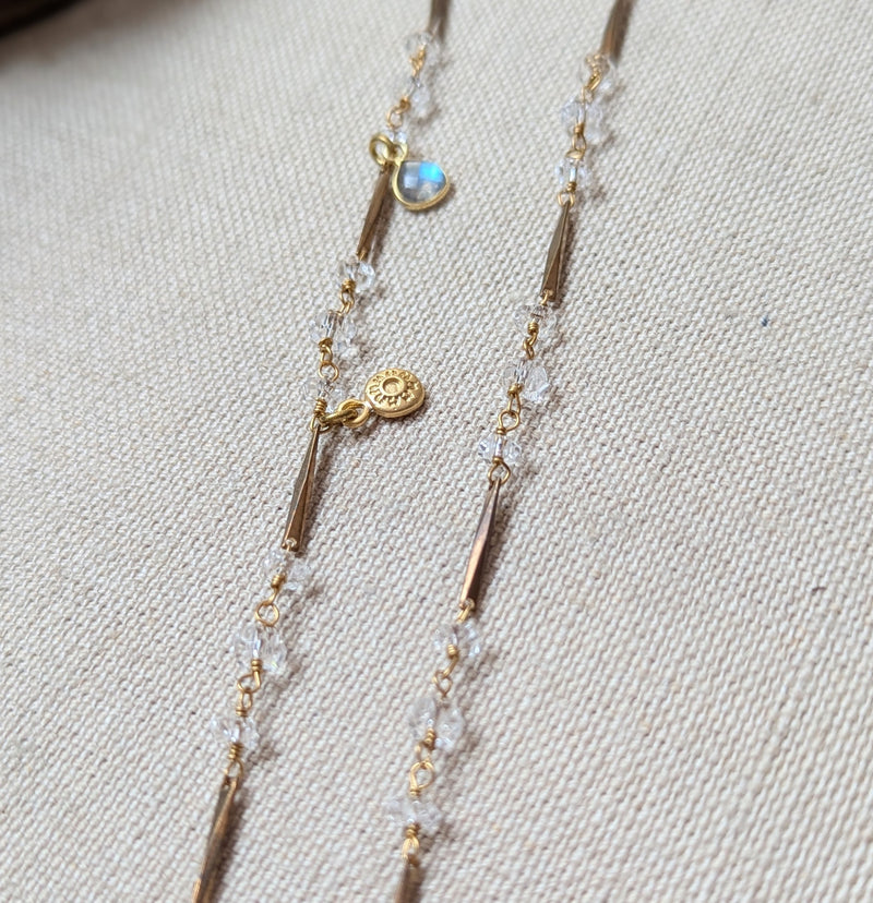 Brass necklace with crystal accents and a glass and brass Poppy pendant on a textured surface