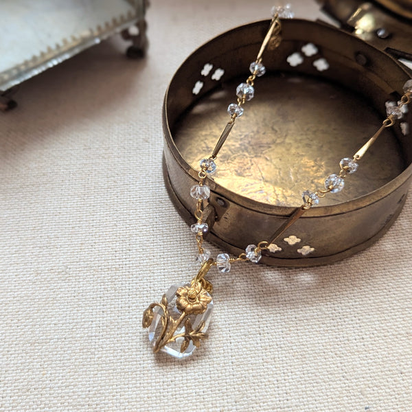 Brass necklace with crystal accents and a glass and brass Poppy pendant on a textured surface