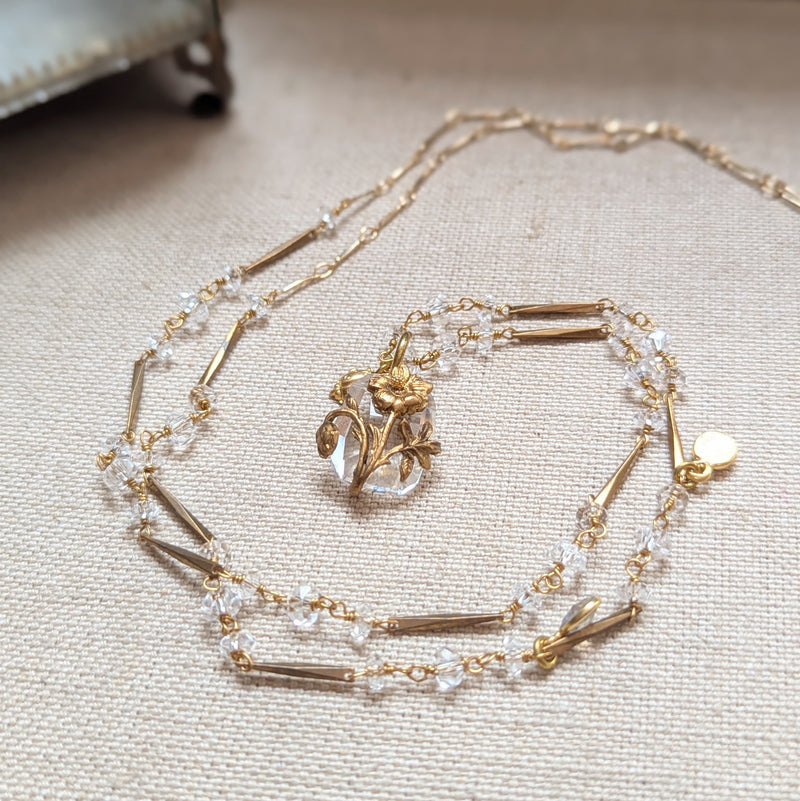 Brass necklace with crystal accents and a glass and brass Poppy pendant on a textured surface
