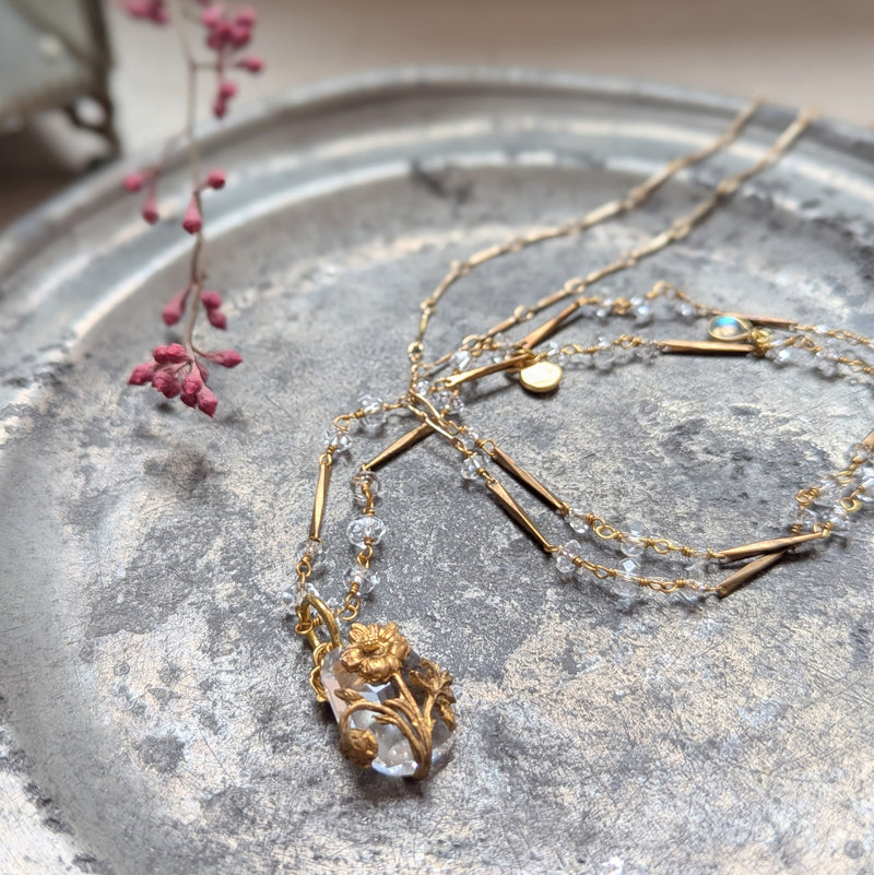 Brass necklace with crystal accents and a glass and brass Poppy pendant on a textured surface