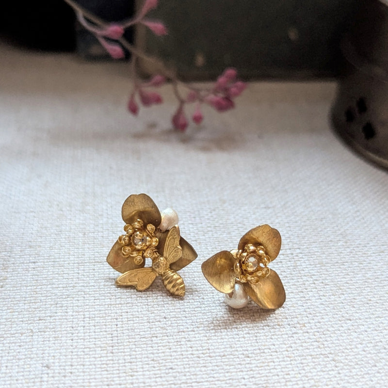 Brass flower and bee earrings with pearl and crystal accents on a textured surface