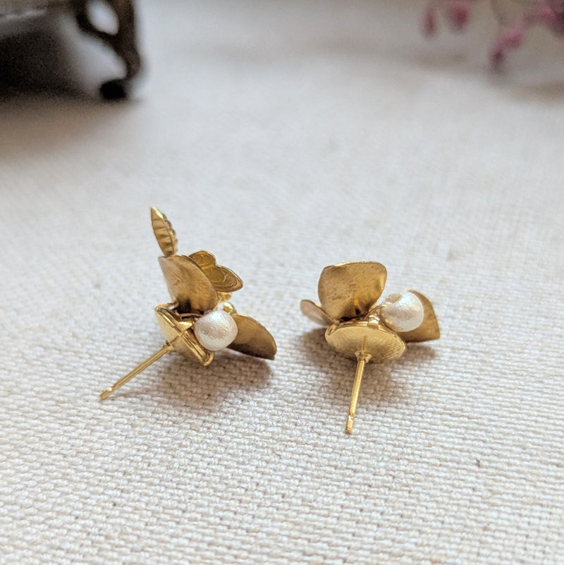 Back of brass flower and bee earrings with pearl and crystal accents on a textured surface