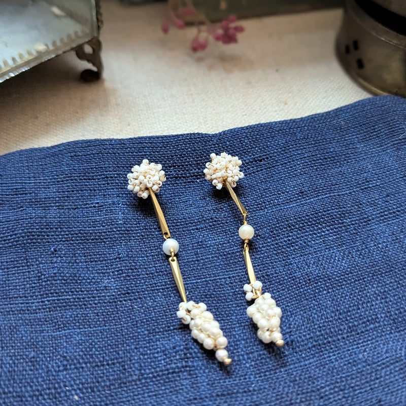 Pair of brass, white bead, and  wood pearl dangle earrings on a textured surface