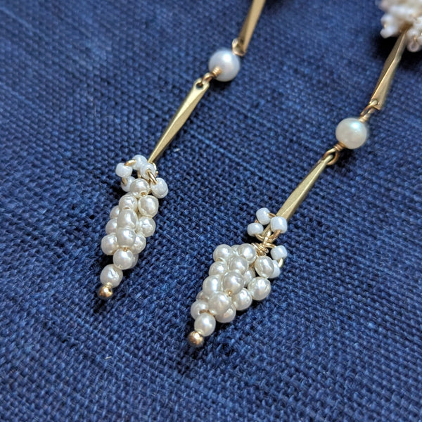 Pair of brass, white bead, and  wood pearl dangle earrings on a textured surface