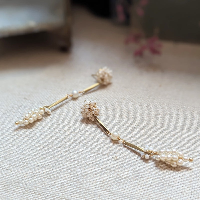 Pair of brass, white bead, and  wood pearl dangle earrings on a textured surface