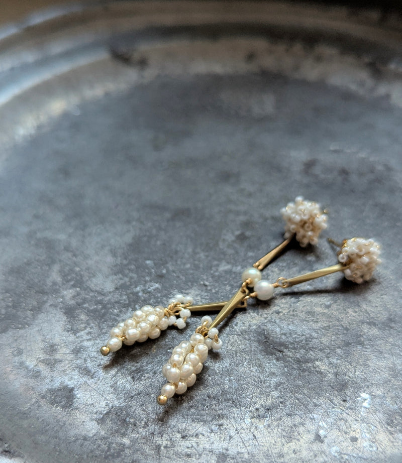 Pair of brass, white bead, and  wood pearl dangle earrings on a metal surface
