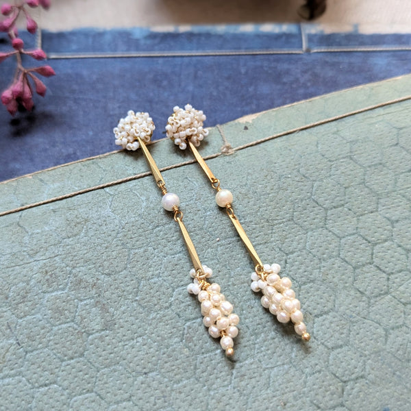 Pair of brass, white bead, and  wood pearl dangle earrings on a textured surface
