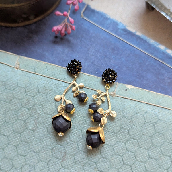 Brass and black beaded earrings inspired by honeysuckle on a textured surface 