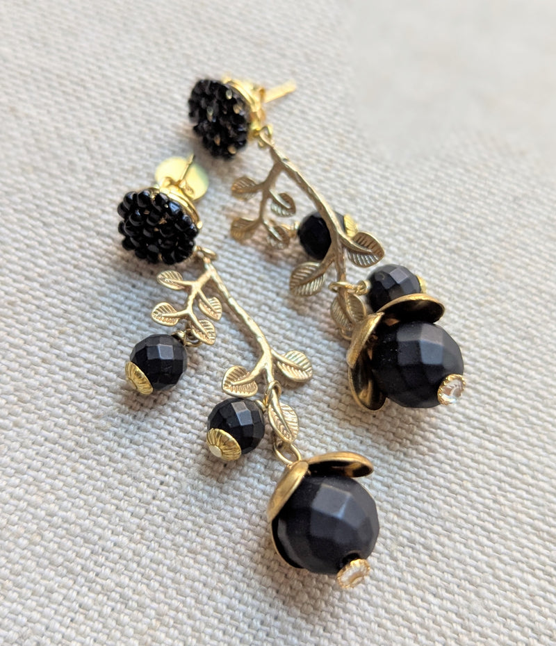 Brass and black beaded earrings inspired by honeysuckle on a textured surface 
