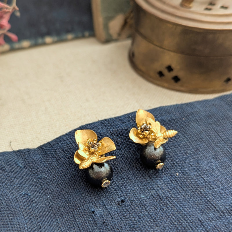 Brass bee and begonia blossom earrings on a texutred linen surface with a blurred background