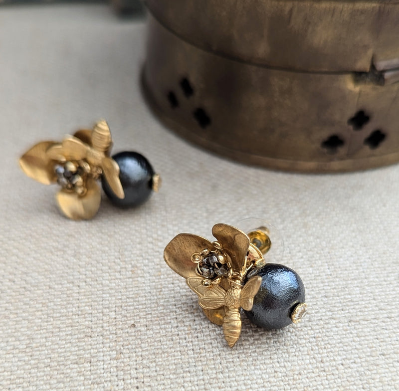 Brass bee and begonia blossom earrings on a texutred linen surface with a blurred background