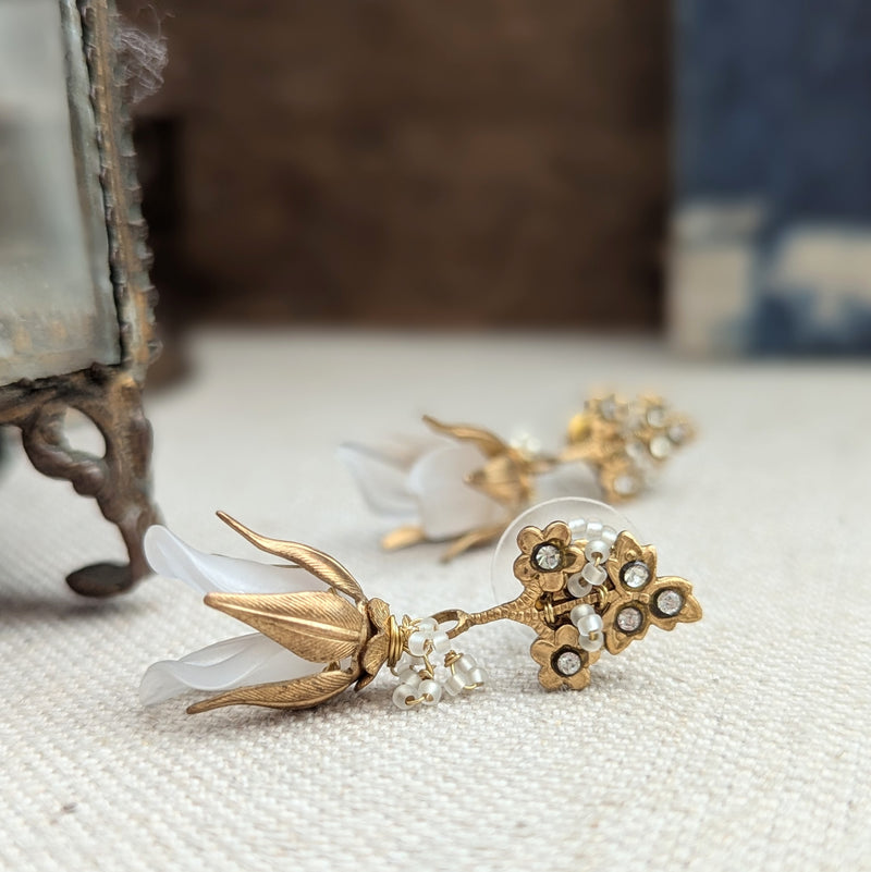 Brass, crystal, and lucite dangle earrings inspired by sweet pea blossoms on a textured background