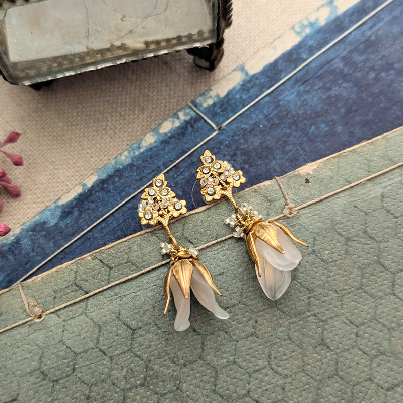 Brass, crystal, and lucite dangle earrings inspired by sweet pea blossoms on a textured background