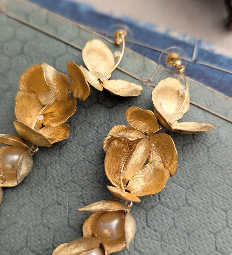 Close up of long chandelier earrings with hanging brass petals and pearl accents 