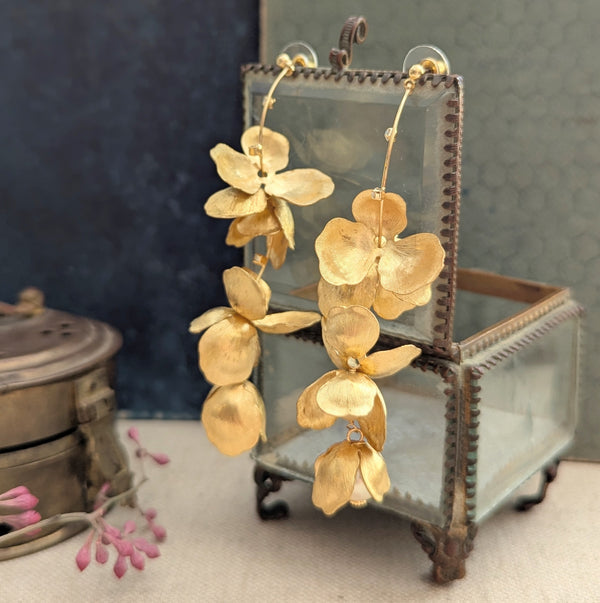 Long chandelier earrings with hanging brass petals and pearl accents on a glass jewelry box.