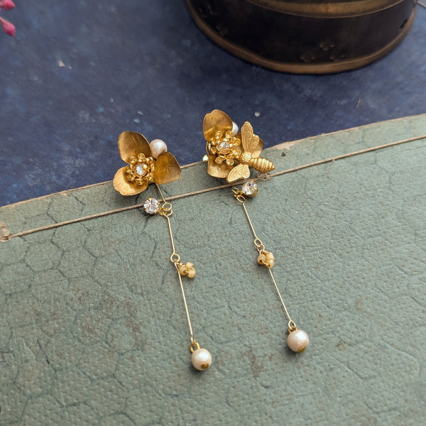 Brass flower and bee dangle earrings with pearl abd crystal accents on a textured surface