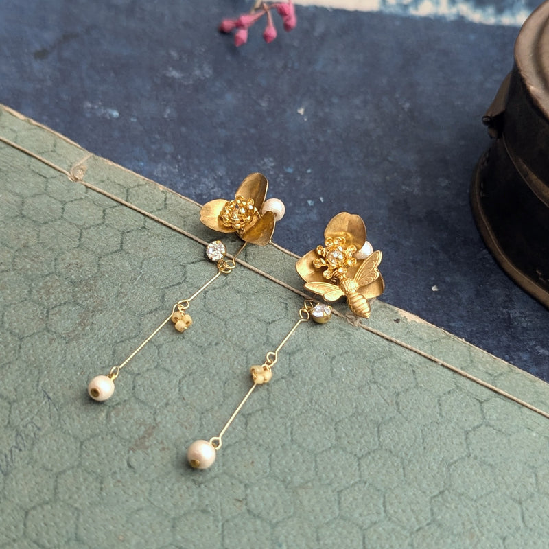 Brass flower and bee dangle earrings with pearl abd crystal accents on a textured surface