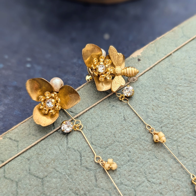 Brass flower and bee dangle earrings with pearl abd crystal accents on a textured surface