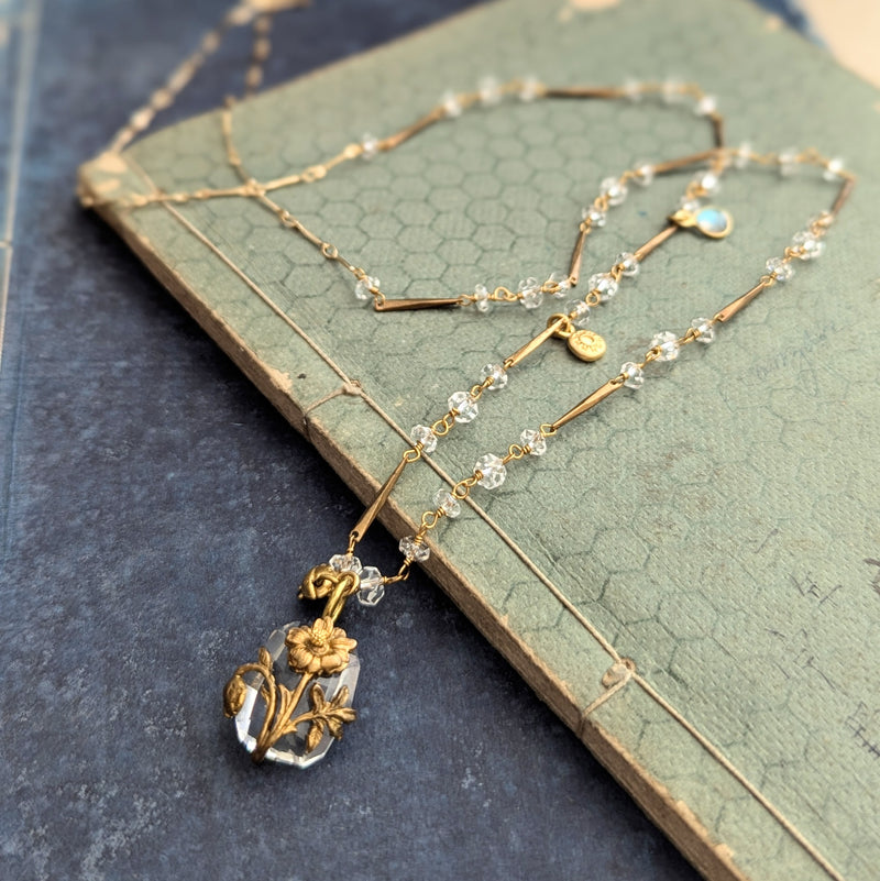 Brass necklace with crystal accents and a glass and brass Poppy pendant on a textured surface
