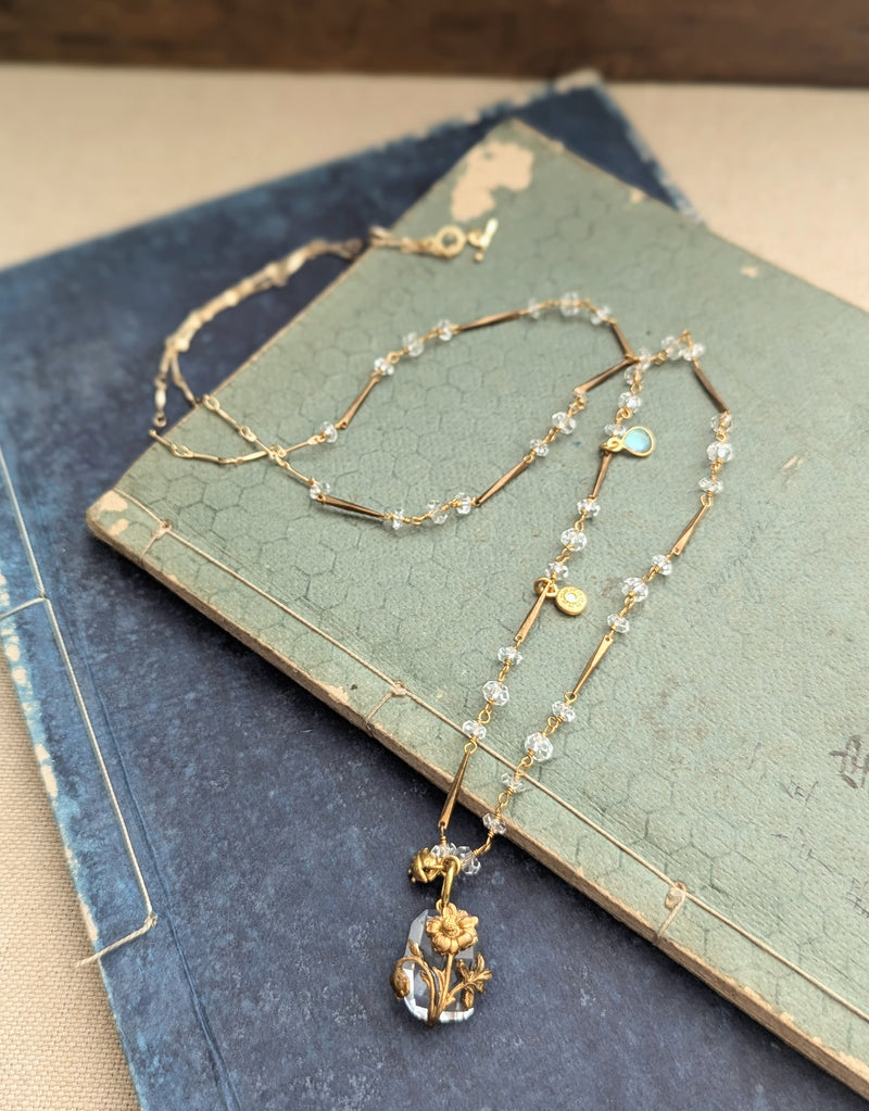 Brass necklace with crystal accents and a glass and brass Poppy pendant on a textured surface
