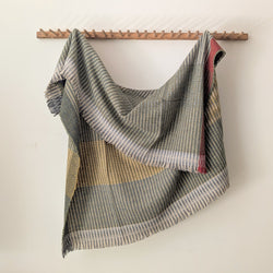 Plaid wool blanket draped over a wooden rack against a white wall