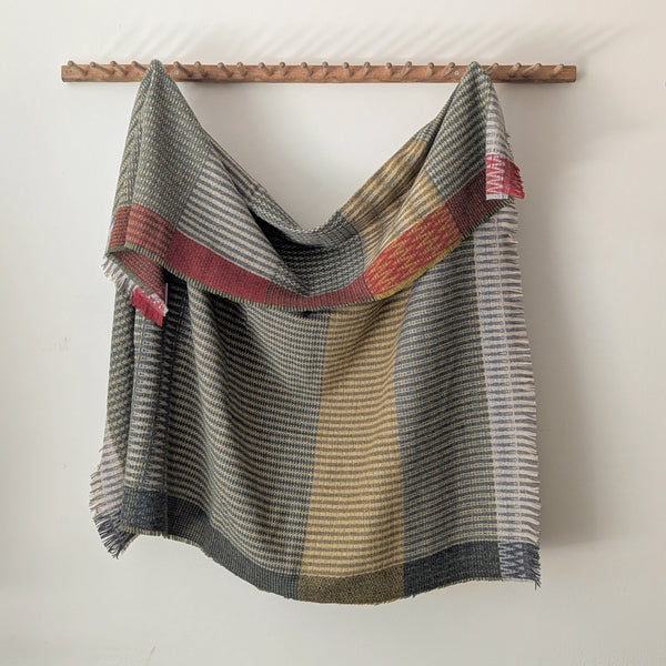Textured blanket with geometric pattern draped over a wooden rod on a white background