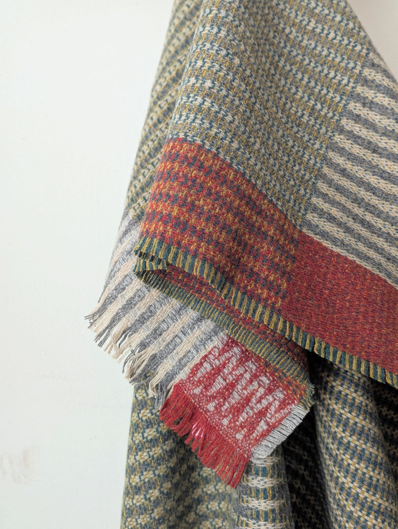 patterned wool blanket draped over a wooden rack against a white wall