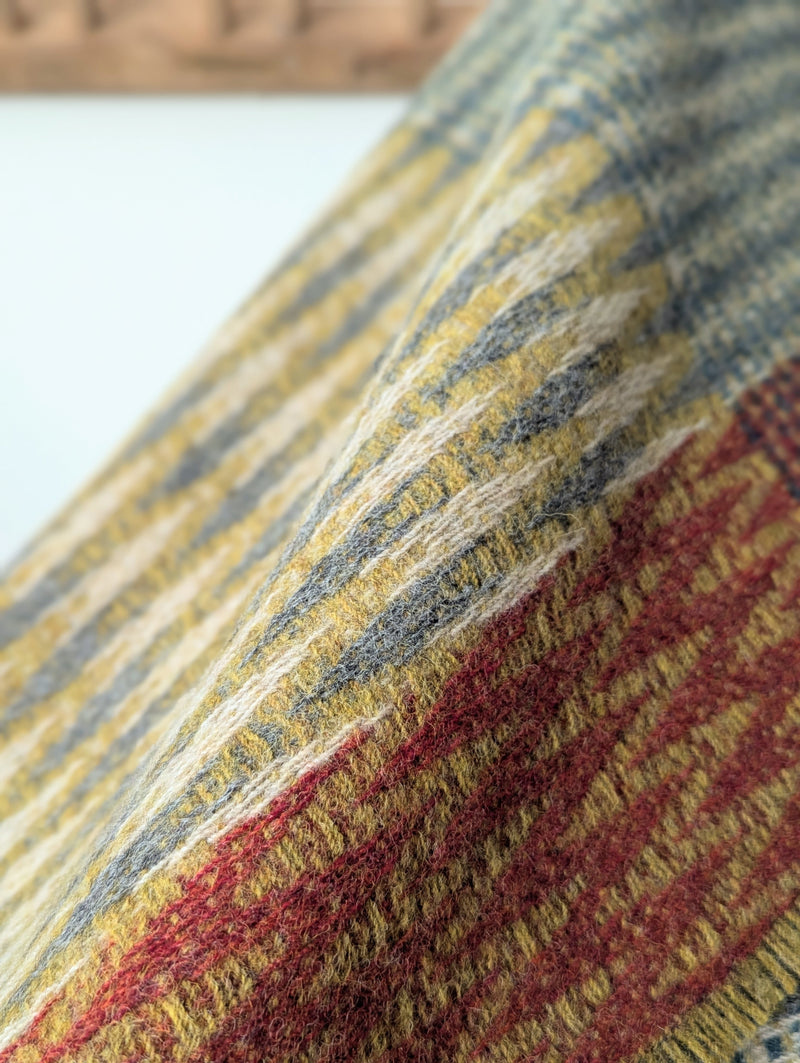 colorful patterned wool blanket draped over a wooden rack against a white wall