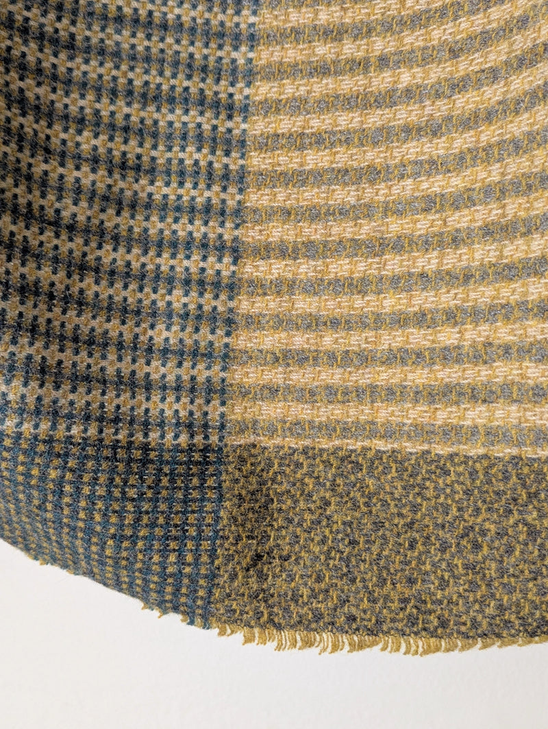 patterned  green blue and yellow wool blanket against a white wall