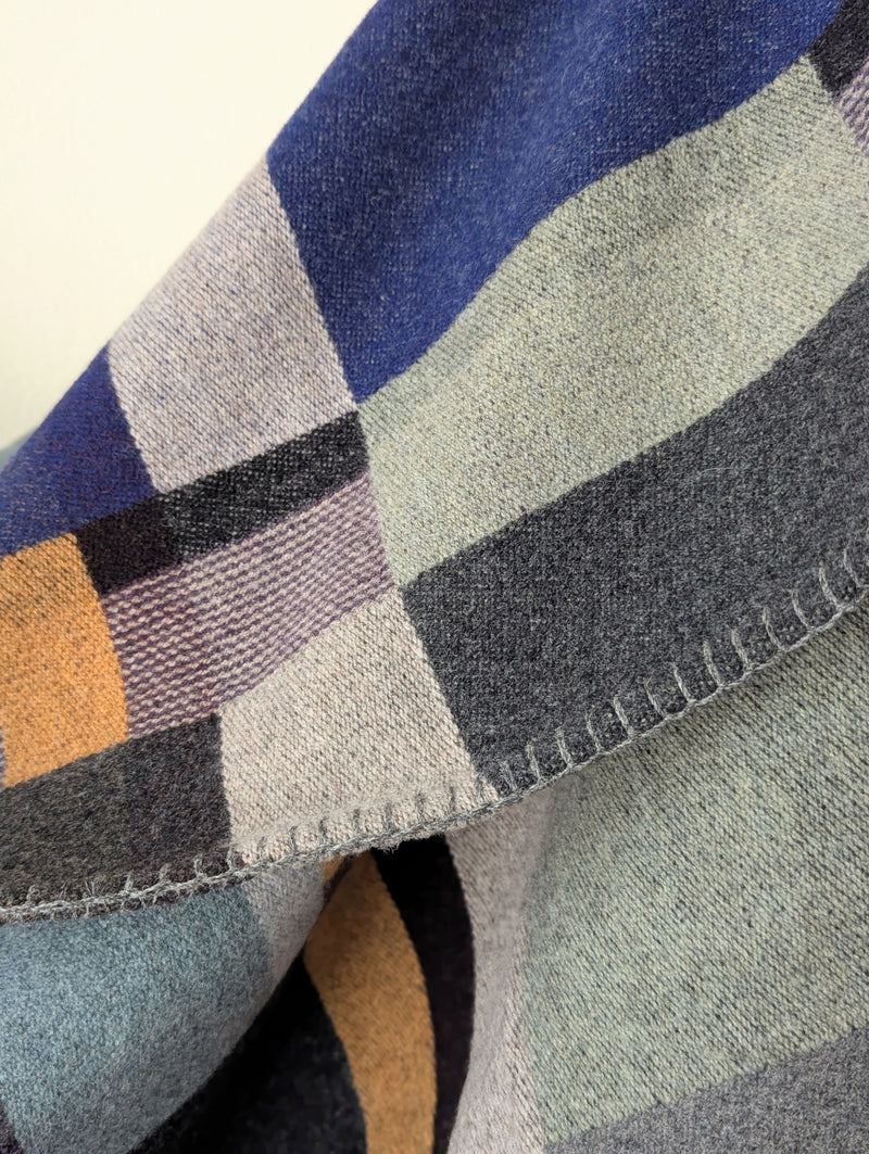 Blue and Gray plaid blanket hanging against a white background