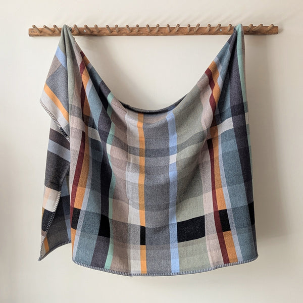 Multicolored blanket hanging on wooden rack against a white background.