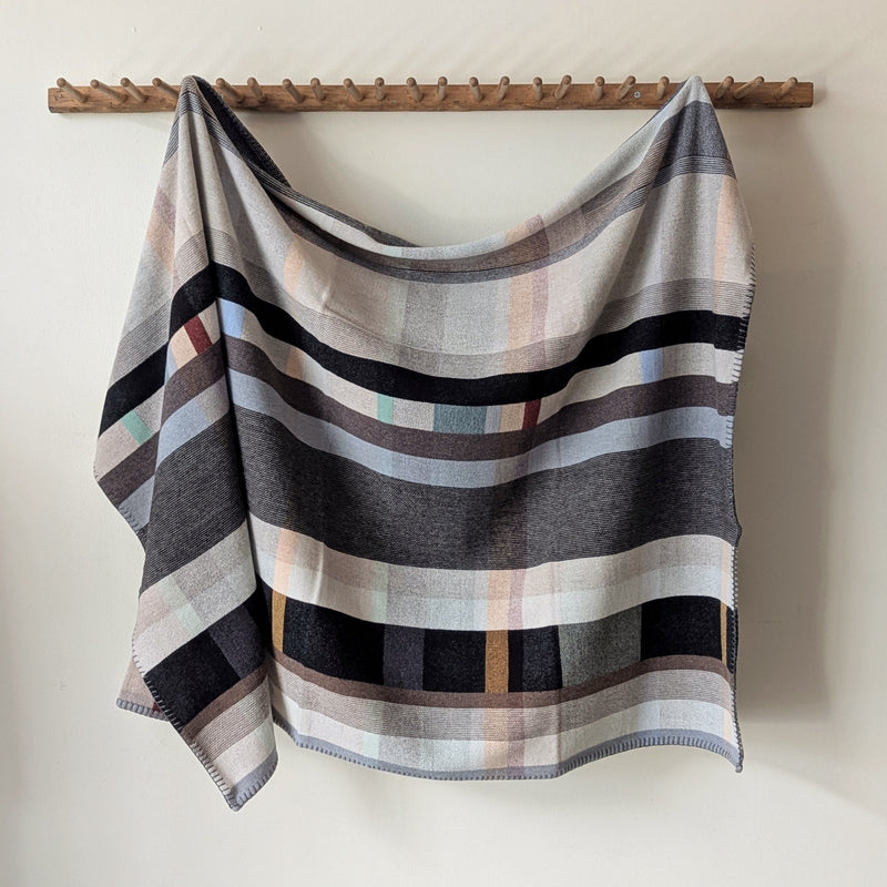 Multicolored blanket hanging on wooden rack against a white background.