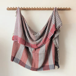 Plaid blanket draped over a wooden rack against a white wall