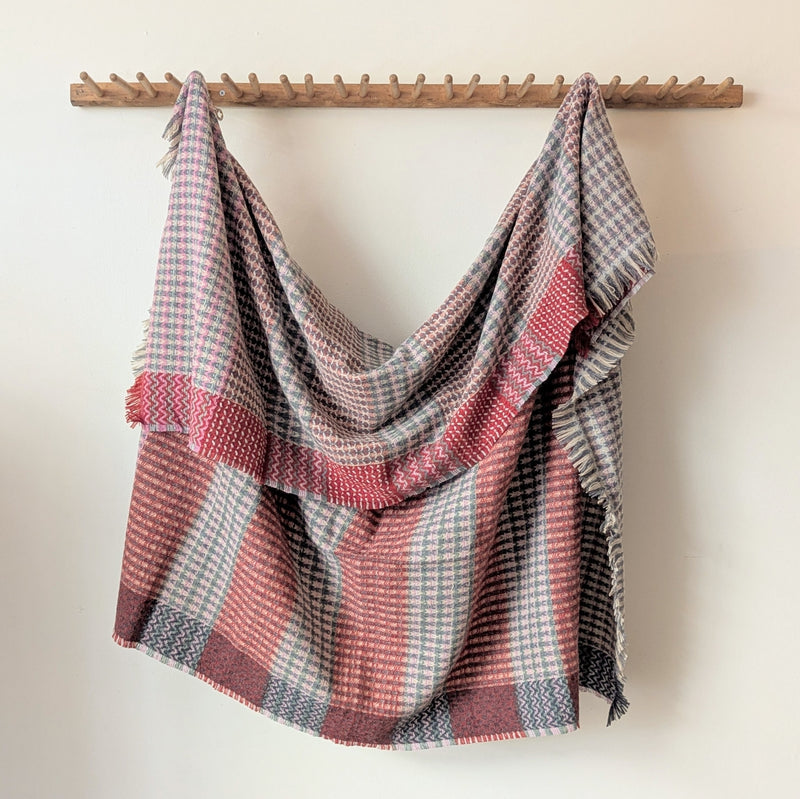 Plaid blanket draped over a wooden rack against a white wall
