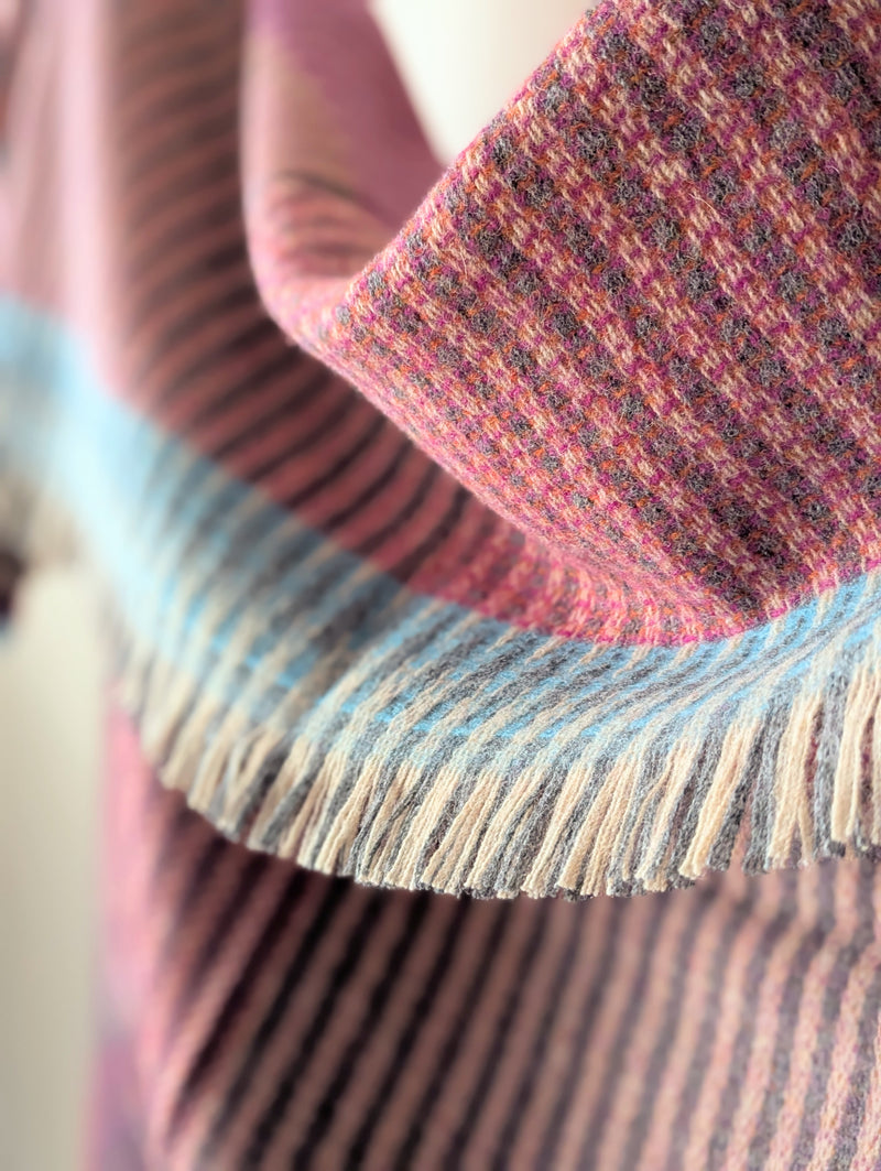 Close-up of a textured fabric with a fringe edge, featuring pink and blue colors.