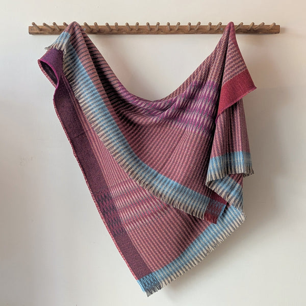 Plaid blanket draped over a wooden rod on a white wall