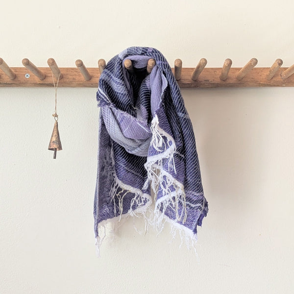 Purple and white scarf hanging on a wooden rack against a white wall.