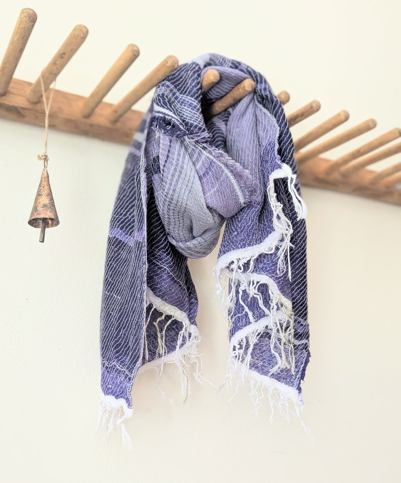Purple and white scarf hanging on a wooden rack against a white wall.